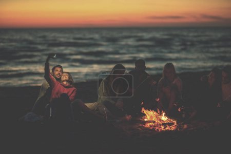Téléchargez les photos : Un groupe d'amis profitant d'un feu de joie sur la plage - en image libre de droit