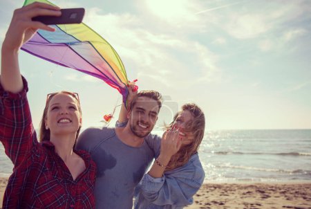 Téléchargez les photos : Groupe d'amis faisant du selfie sur la plage pendant la journée d'automne - en image libre de droit