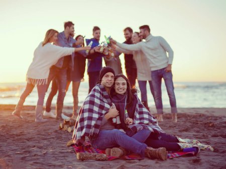Foto de Pareja disfrutando con amigos en la playa al atardecer - Imagen libre de derechos