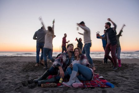 Foto de Pareja disfrutando con amigos en la playa al atardecer - Imagen libre de derechos