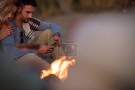 Foto de Grupo de jóvenes amigos sentados junto al fuego en la playa - Imagen libre de derechos
