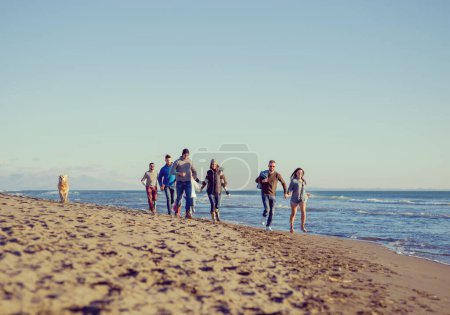 Téléchargez les photos : Groupe d'amis courant sur la plage pendant la journée d'automne - en image libre de droit