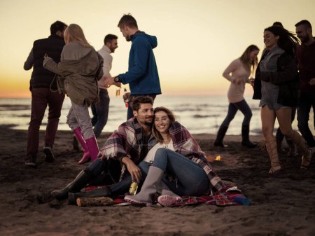 Foto de "Pareja disfrutando con amigos al atardecer en la playa" - Imagen libre de derechos