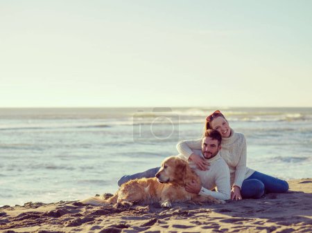 Foto de Pareja con perro disfrutando del tiempo en la playa - Imagen libre de derechos