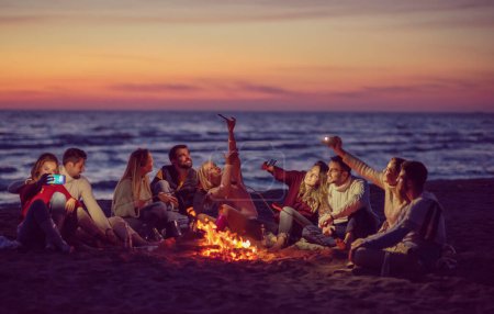 Téléchargez les photos : Groupe d'amis profitant du feu de joie sur la plage - en image libre de droit