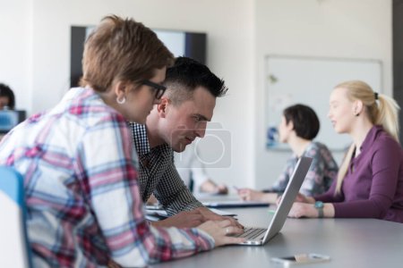 Téléchargez les photos : Jeune couple d'affaires travaillant sur ordinateur portable, groupe d'hommes d'affaires sur la réunion en arrière-plan - en image libre de droit