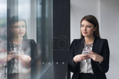 Foto de Chica de negocios de pie en un edificio moderno cerca de la ventana con teléfono - Imagen libre de derechos