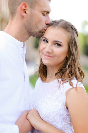Photo for Happy groom kissing bride and holding hands outside. - Royalty Free Image