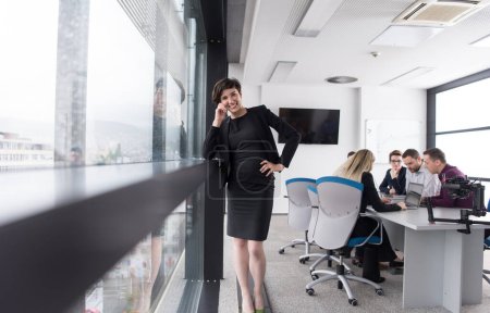 Téléchargez les photos : Femme élégante utilisant le téléphone portable par fenêtre dans un immeuble de bureaux - en image libre de droit