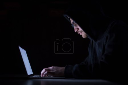 Téléchargez les photos : Pirate utilisant un ordinateur portable tout en travaillant dans le bureau sombre - en image libre de droit