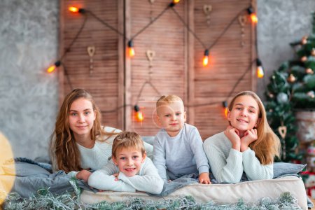 Téléchargez les photos : Joyeux enfants frères et sœurs qui s'amusent sur le lit près du sapin de Noël le matin de Noël - en image libre de droit