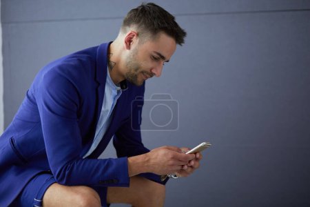 Téléchargez les photos : "Jeune homme d'affaires assis sur les toilettes avec téléphone isolé sur le fond." - en image libre de droit