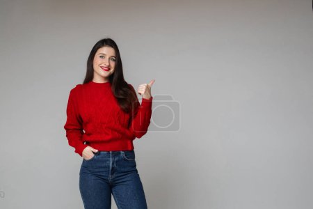 Photo for Woman in warm red sweater and blue jeans keeps her hand in the pocket - Royalty Free Image