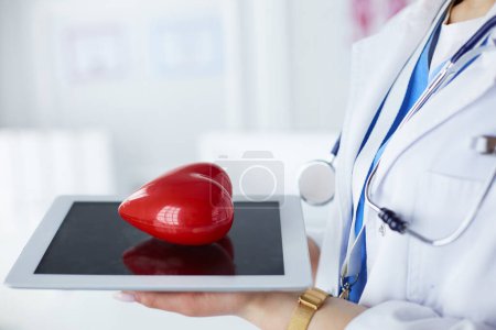 Photo for "Female doctor with stethoscope holding heart on tablet - Royalty Free Image