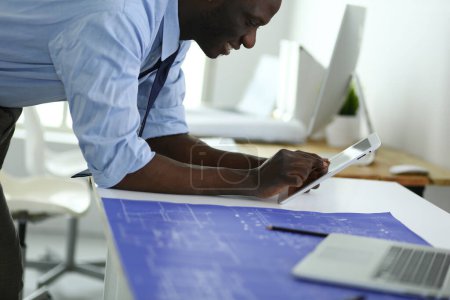 Téléchargez les photos : Architecte afro-américain travaillant avec l'ordinateur et les plans dans le bureau - en image libre de droit