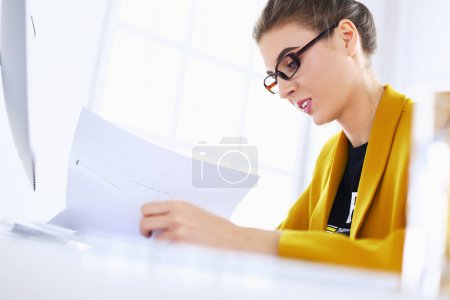 Téléchargez les photos : Belle jeune femme d'affaires faisant de la paperasse tout en étant assis au bureau devant un ordinateur portable - en image libre de droit
