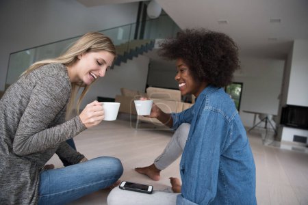 Téléchargez les photos : Jeunes femmes multiethniques assises sur le sol et buvant du café - en image libre de droit