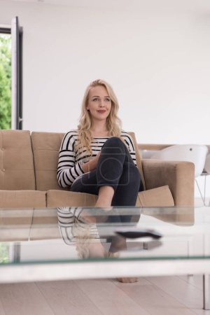 Photo for Young woman sitting on sofa with mobile phone - Royalty Free Image