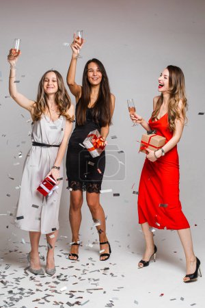Foto de Three girls with drinks having fun under confetti. - Imagen libre de derechos