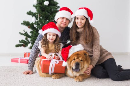 Foto de Mascotas, vacaciones y concepto festivo - Familia con perro están sentados en el suelo cerca del árbol de Navidad
. - Imagen libre de derechos