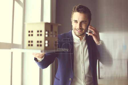 Photo for "Businessman holding house miniature on hand standing in office." - Royalty Free Image