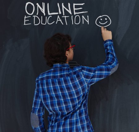 Photo for Teen Boy with chalk  writing on black chalkboard online education - Royalty Free Image