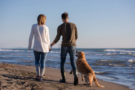 Téléchargez les photos : Couple avec chien s'amuser sur la plage le jour d'automne - en image libre de droit