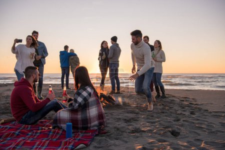 Téléchargez les photos : Couple profiter avec des amis au coucher du soleil sur la plage - en image libre de droit