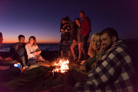 Téléchargez les photos : Couple profiter avec des amis au coucher du soleil sur la plage - en image libre de droit