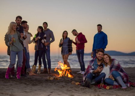 Téléchargez les photos : Couple profitant de feu de joie avec des amis sur la plage - en image libre de droit