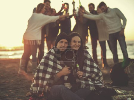 Foto de Pareja disfrutando con amigos al atardecer en la playa - Imagen libre de derechos