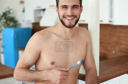 Foto de Cepillarse los dientes por la mañana. Guapo joven barba hombre cepillándose los dientes y sonriendo. - Imagen libre de derechos
