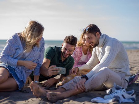 Téléchargez les photos : Groupe d'amis s'amuser sur la plage pendant la journée d'automne - en image libre de droit