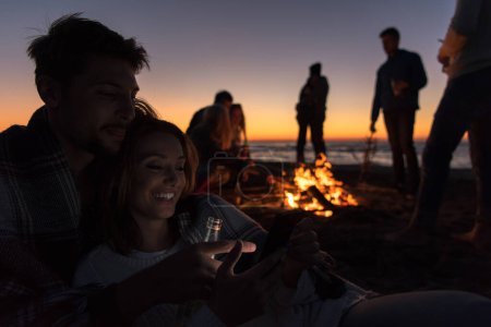 Foto de Pareja disfrutando de la hoguera con amigos en la playa - Imagen libre de derechos