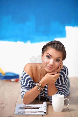 Photo for Portrait of female painter lying on floor near wall after paintingand holding a cup - Royalty Free Image