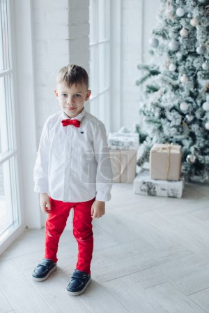 Téléchargez les photos : Petit garçon caucasien assis près de l'arbre de Noël avec un cadeau - en image libre de droit