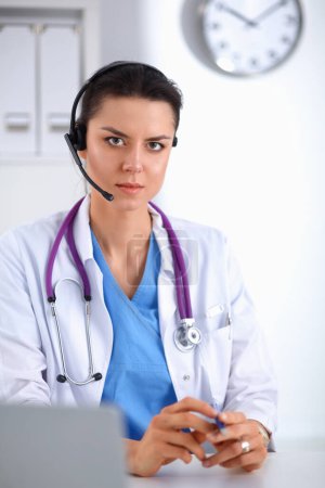 Foto de Doctor con auriculares sentados detrás de un escritorio con portátil sobre fondo gris - Imagen libre de derechos