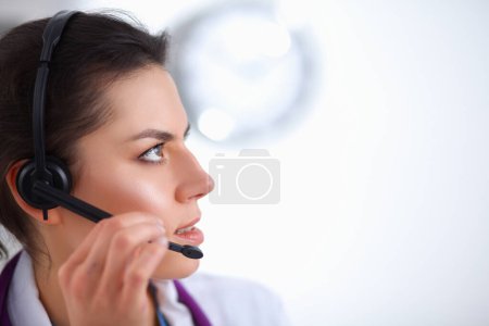 Téléchargez les photos : Médecin portant casque assis derrière un bureau avec ordinateur portable sur fond gris - en image libre de droit