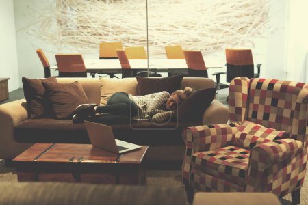 Téléchargez les photos : Femme dormant sur un canapé dans un bureau créatif - en image libre de droit