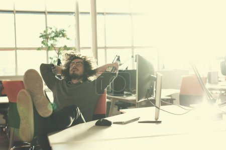 Téléchargez les photos : Jeune homme d'affaires assis avec les jambes sur le bureau au bureau - en image libre de droit