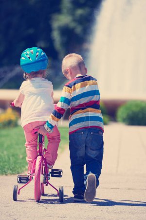 Photo for Boy and girl in park learning to ride a bike - Royalty Free Image