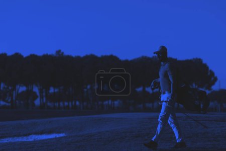 Téléchargez les photos : Golfeur marchant et portant sac de golf au beau coucher de soleil - en image libre de droit