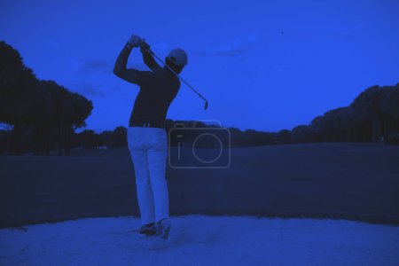 Téléchargez les photos : Golfeur frapper un sable bunker coup au coucher du soleil - en image libre de droit