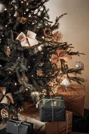 Téléchargez les photos : Livraison des vacances de Noël et concept de cadeaux durables. Boîtes cadeaux noires emballées dans un emballage écologique avec du papier recyclé sous l'arbre de Noël décoré - en image libre de droit