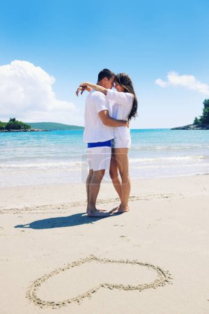 Téléchargez les photos : Couple heureux s'amuser sur la plage avec coeur sur le sable - en image libre de droit