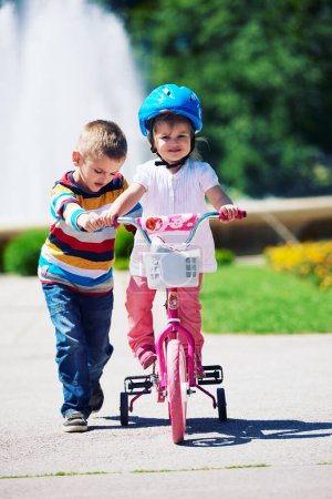 Foto de Niño y niña en el parque aprendiendo a andar en bicicleta - Imagen libre de derechos