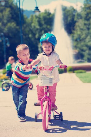 Foto de Niño y niña en el parque aprendiendo a andar en bicicleta - Imagen libre de derechos