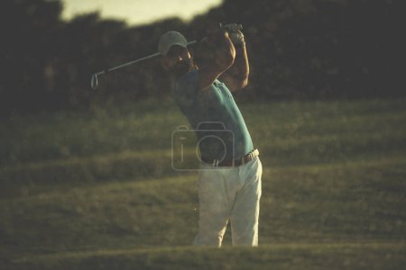 Foto de Golfista golpeando un tiro bunker de arena en la puesta del sol - Imagen libre de derechos