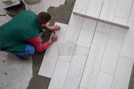 Téléchargez les photos : Travailleur installant les carreaux de céramique effet bois sur le sol - en image libre de droit