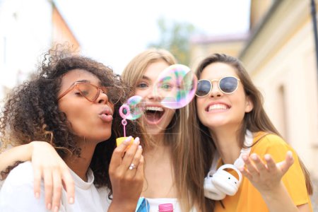 Téléchargez les photos : Trois belles femmes heureuses soufflant des bulles de savon dans la rue de la ville
. - en image libre de droit